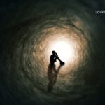 Silhouette of a person sitting in the center of a dark, circular tunnel with a bright light at the end.
