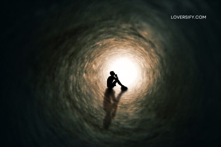 Silhouette of a person sitting in the center of a dark, circular tunnel with a bright light at the end.
