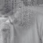 Monochromatic close-up of a couple embracing through a steamy, water-droplet-covered window.