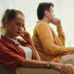 A woman and a man sit apart on a couch, both appearing pensive.