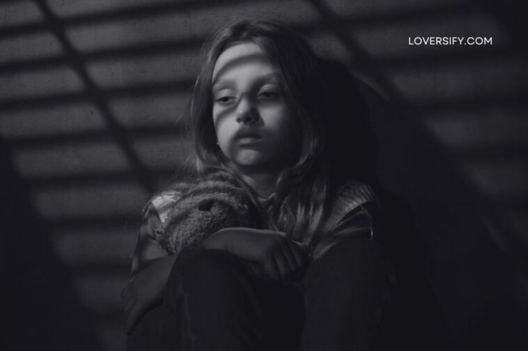 A young girl in black and white clutches a stuffed animal, looking down as striped shadows fall across her face.