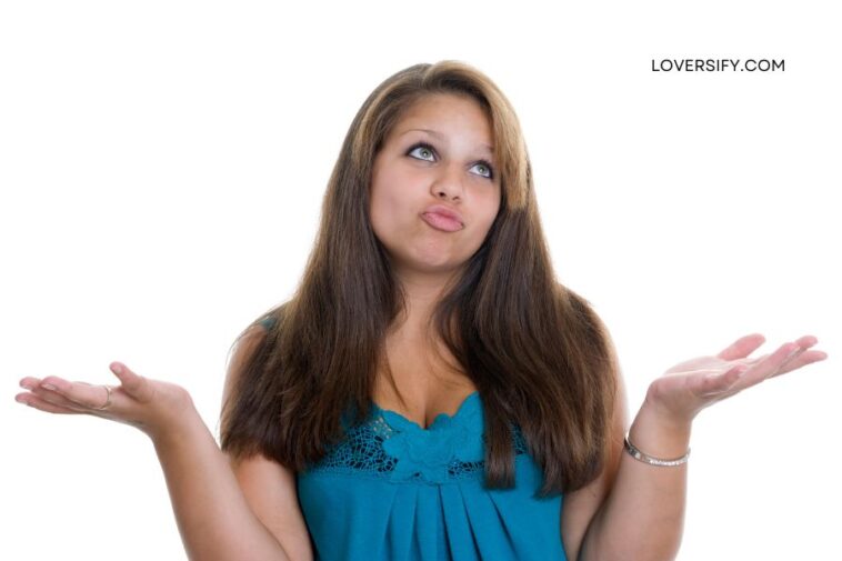 A young woman with long brown hair and a teal top shrugs with her palms up, looking up and to the side with a pursed lip expression against a white background.