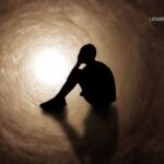 Silhouette of a person sitting with their head in their hands inside a dark, swirling tunnel with bright light at the far end.