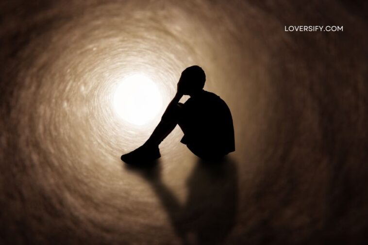 Silhouette of a person sitting with their head in their hands inside a dark, swirling tunnel with bright light at the far end.